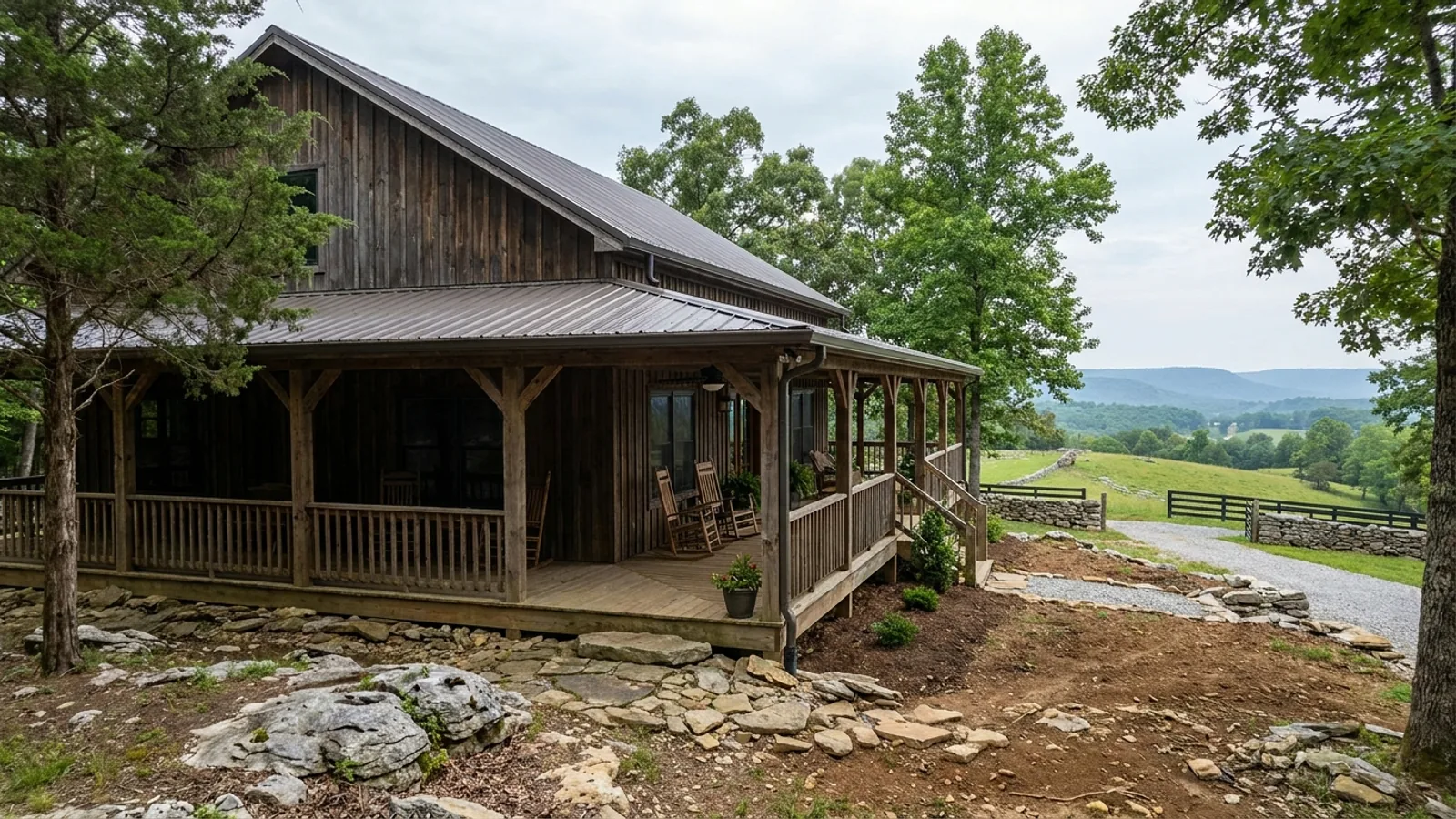A barndominium exterior showing a deep wrap-around covered porch with posts and railing along two sides of the building.