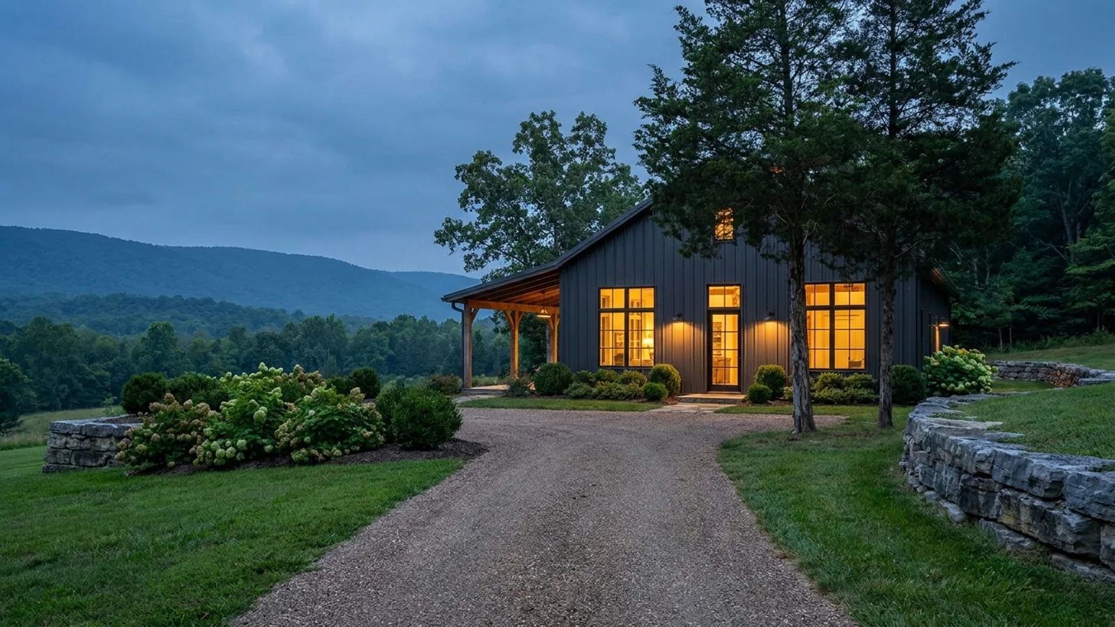A finished barndominium at dusk with warm interior lighting glowing through its large windows.