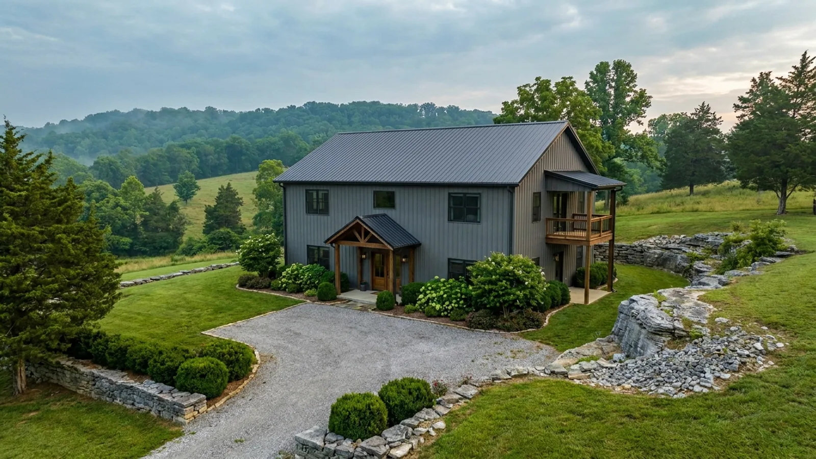 A completed two-story barndominium with visible second-story windows and a small covered balcony above the entry porch.